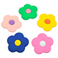 A set of five colorful daisy flower charms in pink, purple, yellow, blue, and green, designed to be attached to a charm-ready Crocs shoe or accessory like Cutie Crowns. 