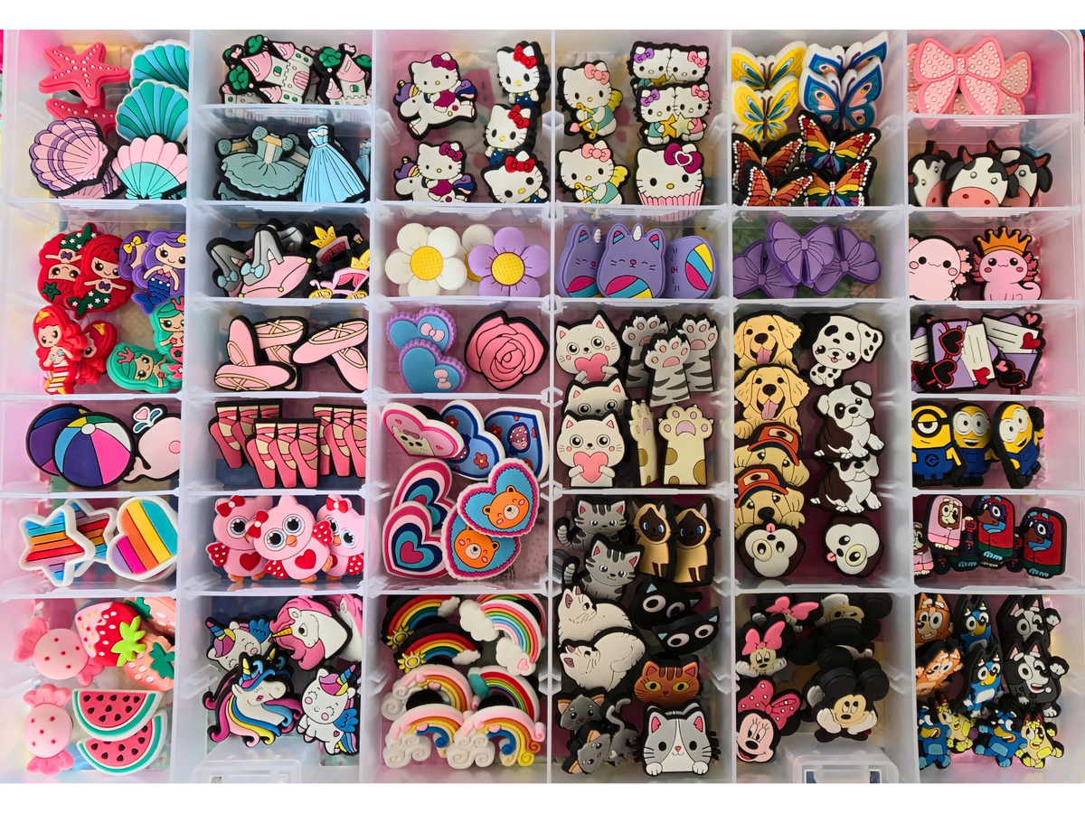 A white plastic organizer tray filled with many small decorative accessories, including Hello Kitty character pieces, bows, flowers, rainbows, animals, and other colorful embellishments, arranged in a grid.